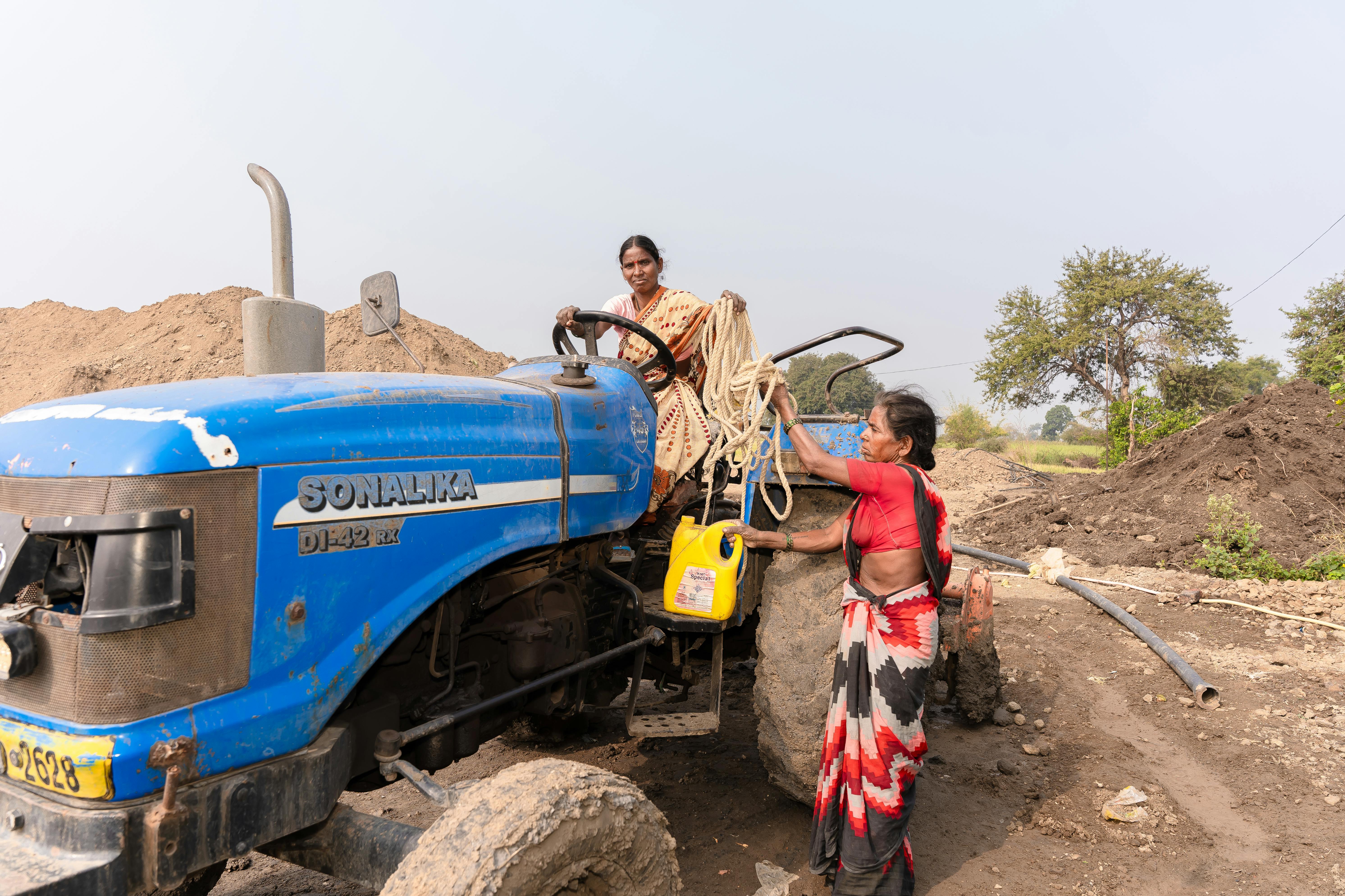 Two women collaborating beside a blue tractor